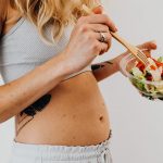 Close-up of a woman in a crop top enjoying a fresh salad indoors.